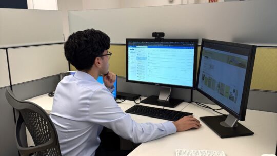 An intern looks at the monitors at their desk